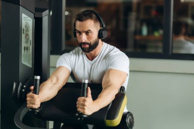 Bodybuilder man doing exercises in fitness club. The guy is wearing a white T-shirt. Fitness healthy lifestyle concept