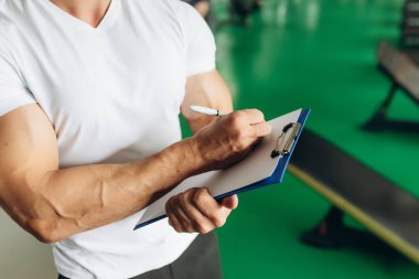 Personal fitness trainer with workout plan close up in gym background. Sport, fitness and healthy life style concept.