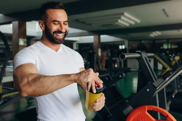 A young man rests after training in the gym, holding a shaker in his hand. Fitness and training concept