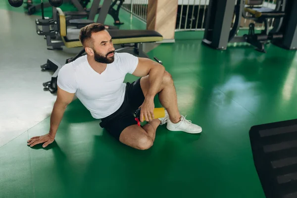 Athletic man in white t-shirt relaxing on gym floor after training