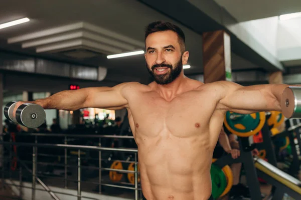 athletic man doing exercises with dumbbells with a bare torso in the gym