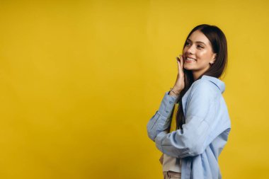 Portrait cute smiling classic dressed student girl looking directly to the camera and pointing with her index finger to the left side, isolated over yellow background. Copy space