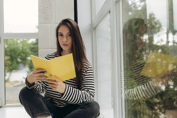 Young Caucasian Girl Sits Windowsill Bright Room Enthusiastically Reads Book — Foto de Stock