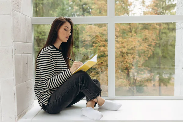 Portrait Attractive Girl Sitting Windowsill Doing Homework Notebook — Stok fotoğraf