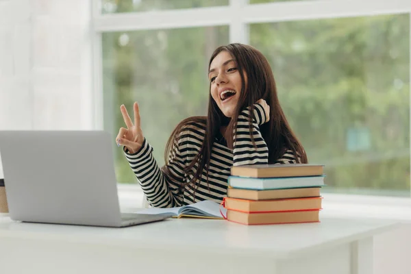 Smiling girl student study online with laptop, happy young woman learn language listen lecture watch webinar write notes look at laptop sit in home, distance education.