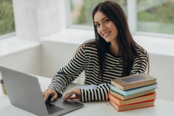 Portrait of pretty young woman studying sitting at table with laptop and books at home. Learning concept