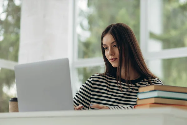 Portrait of pretty young woman studying sitting at table with laptop and books at home. Learning concept