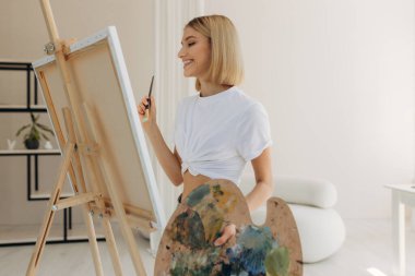The artist paints in the studio. Attractive girl wearing a white T-shirt