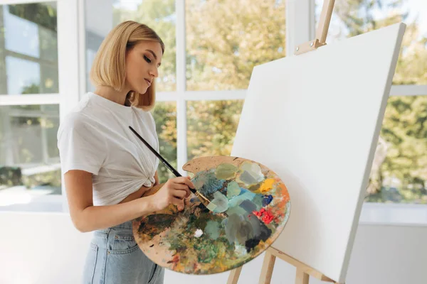 The artist paints in the studio. Attractive girl wearing a white T-shirt