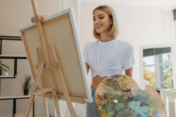 The artist paints in the studio. Attractive girl wearing a white T-shirt