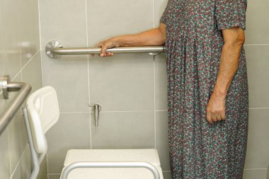 Asyalı yaşlı kadın hasta tuvalette tuvalet desteğini, tırabzan emniyet çubuğunu, hemşire hastanesinde güvenliği kullanıyor..                       