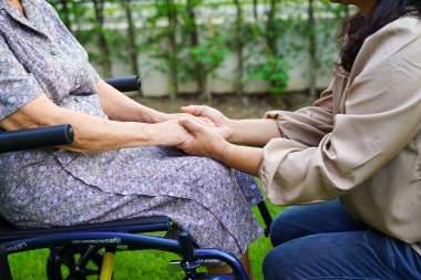 Bakıcı, parkta tekerlekli sandalyede oturan Asyalı yaşlı kadın maluliyet hastasına yardım ediyor..