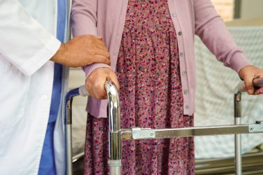 Doktor, Asyalı yaşlı kadın engelli hastaya hemşirelik hastanesinde Walker 'la birlikte yürümesi için yardım ediyor..