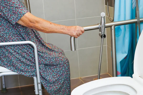 Asyalı yaşlı kadın hasta tuvalette tuvalet desteğini, tırabzan emniyet çubuğunu, hemşire hastanesinde güvenliği kullanıyor..                    
