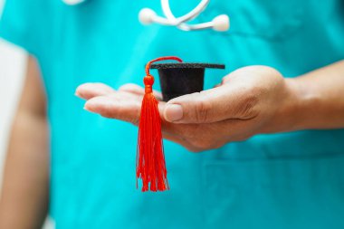 Asian woman doctor holding graduation hat in hospital, Medical education concept.