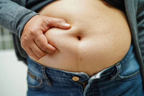 Şişman Asyalı kadın şişman göbeğini sıkmak için elini kullanıyor. Büyük boy aşırı kilolu ve obez..