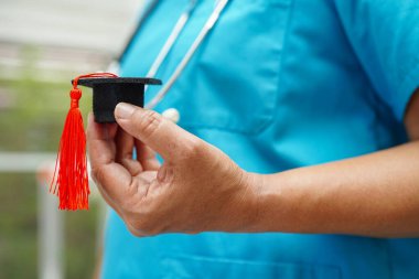 Asian woman doctor holding graduation hat in hospital, Medical education concept.