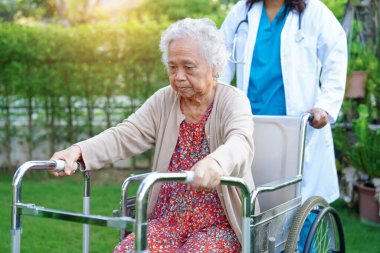 Doktor, Asyalı yaşlı kadın engelli hastaya parkta yürüme konusunda yardım ediyor..