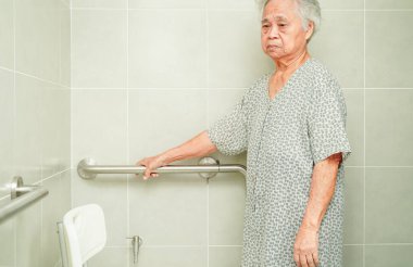 Asyalı yaşlı kadın hasta tuvalette tuvalet desteğini, tırabzan emniyet çubuğunu, hemşire hastanesinde güvenliği kullanıyor..