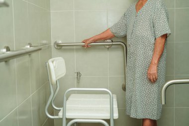 Asyalı yaşlı kadın hasta tuvalette tuvalet desteğini, tırabzan emniyet çubuğunu, hemşire hastanesinde güvenliği kullanıyor..