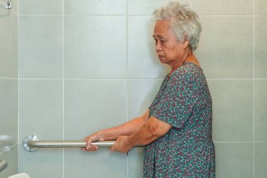 Asyalı yaşlı kadın hasta tuvalette tuvalet desteğini, tırabzan emniyet çubuğunu, hemşire hastanesinde güvenliği kullanıyor..