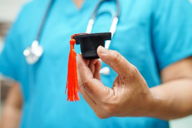 Asian woman doctor holding graduation hat in hospital, Medical education concept.