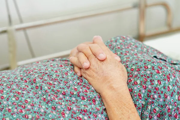 Asian elder senior woman patient holding bed rail while lie down with hope waiting her family in hospital.