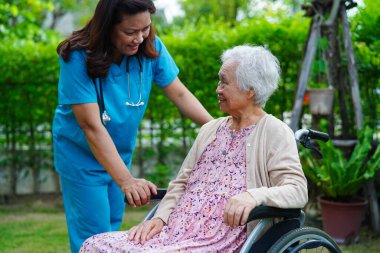 Doktor, parkta tekerlekli sandalyede oturan Asyalı yaşlı kadın engelli hastaya yardım ediyor. Tıbbi konsept..