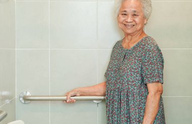 Asyalı yaşlı kadın hasta tuvalette tuvalet desteğini, tırabzan emniyet çubuğunu, hemşire hastanesinde güvenliği kullanıyor..