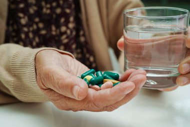 Elinde bardakta su olan hap tutan Asyalı yaşlı bir kadın. Güçlü, sağlıklı bir tıbbi konsept..