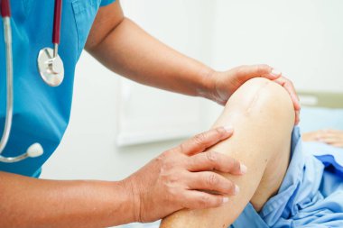 Doktor, hastanede dizinde yara izi olan Asyalı yaşlı kadın hastayı kontrol ediyor..