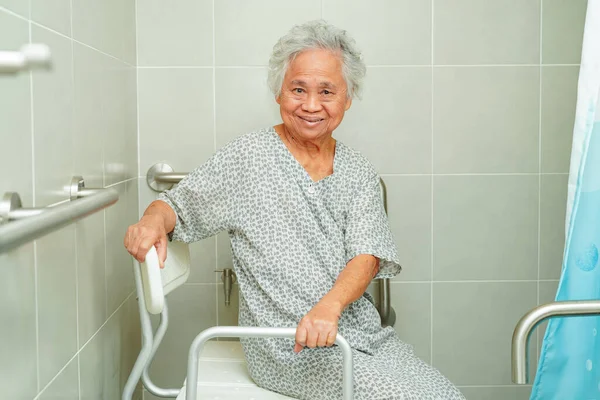 Asian elderly old woman patient use toilet support rail in bathroom, handrail safety grab bar, security in nursing hospital.