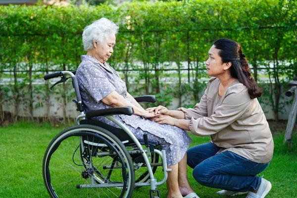 Caregiver help Asian elderly woman disability patient sitting on wheelchair in park, medical concept.