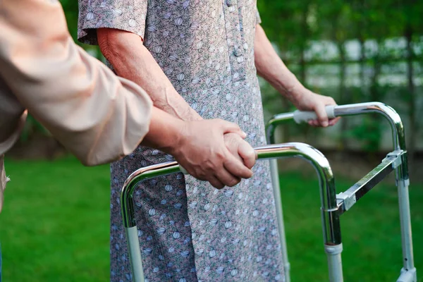 Caregiver help Asian elderly woman disability patient walk with walker in nursing hospital, medical concept.
