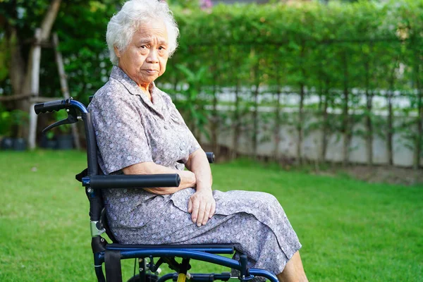 Asian elderly woman disability patient sitting on wheelchair in park, medical concept.