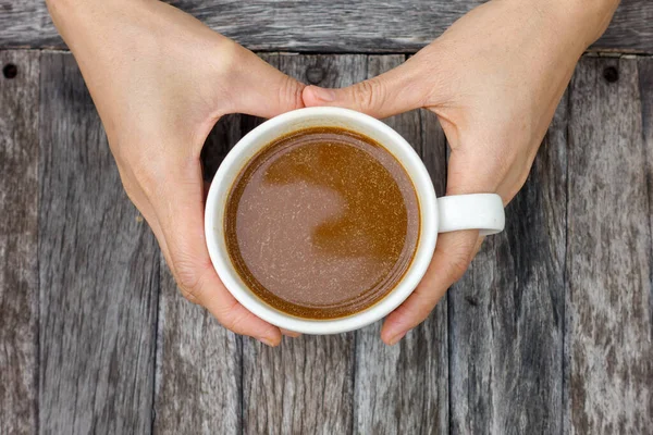 Ahşap masa arkasında siyah bir kahve fincanı tutan el görüntüsü..