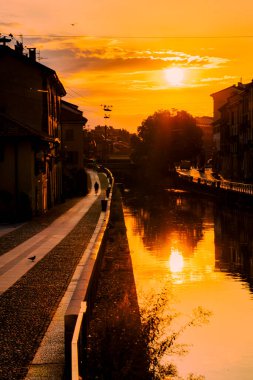 Gün batımında İtalya 'nın Milano kanalları. Rıhtımda gün batımında sıska bir şehir manzarası portakal ve ılık renklerle dolu.
