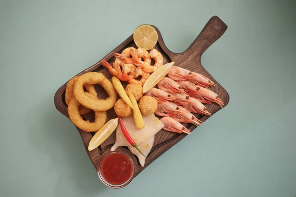 Kızarmış kalamar halkalı deniz ürünleri tabakları, karides ve soğan halkaları, ahşap bir arka planda limonla süslenmiş..