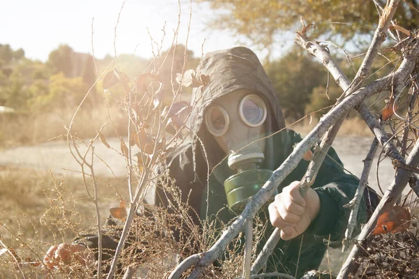 Askeri kadın gaz maskeli dalların arkasında saklanıyor. Kimyasal savaş kavramı. Boşluğu kopyala