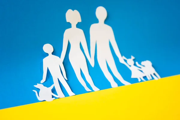 paper cutout of a family fleeing from war. parents with two children and their pets on the colors of the flag of ukraine. welcome refiugees.