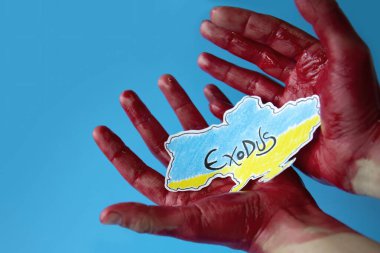 Kanlı eller mavi arka planda Ukrayna haritasının rengine boyanmış kağıdını tutuyor. Sivil vatandaşların toplu göçü.
