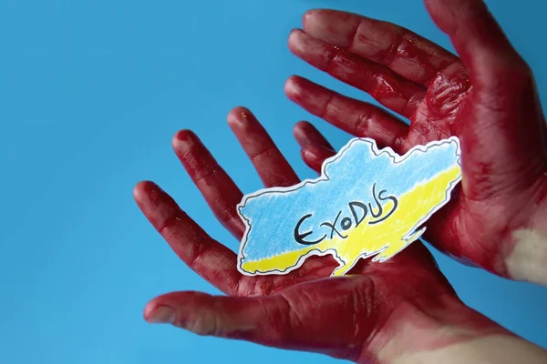 Kanlı eller mavi arka planda Ukrayna haritasının rengine boyanmış kağıdını tutuyor. Sivil vatandaşların toplu göçü.