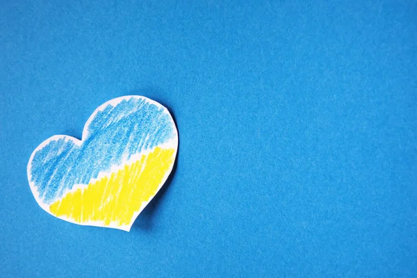 Ukrayna bayrağı renginde mavi arka planı olan kalp şeklinde kağıt kesiği tutan parmaklar. Kopyalamak için boşluk