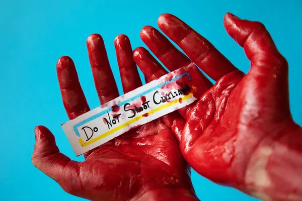 Mavi arka planda Ukrayna bayrağı renklerinde sivillere yapılan saldırıları geri püskürten bir kadının kanlı elleri.