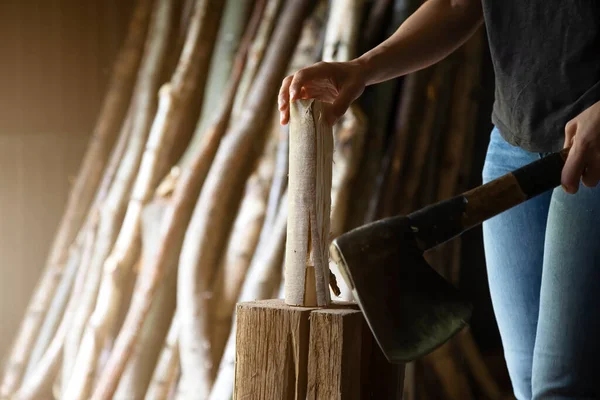 Bir elinde balta, diğer elinde de doğramak için odun olan bir kadının elini yakın plan çek. arkaplandaki günlükler