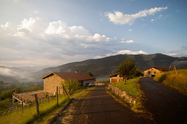 Akşam ışığında Atxondo Vadisi 'nin çiftlik evleri. Gökyüzü bulutlu. Görüntüde turuncu tonlar baskın. Doğa resimleri