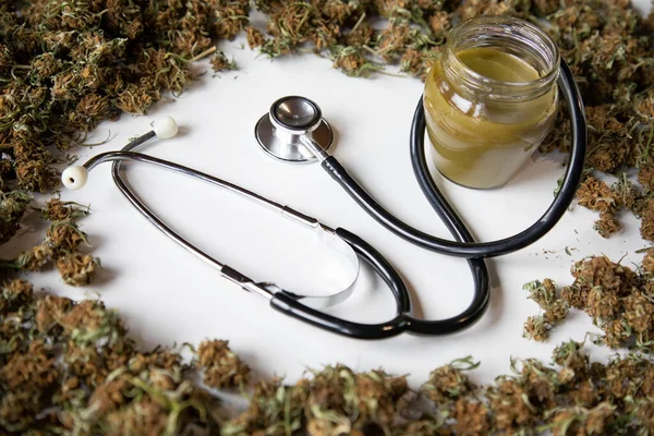 Tıbbi marihuana konsepti, çemberde marihuana tomurcukları, içinde marihuana merhemi ve stetoskop. beyaz arkaplan