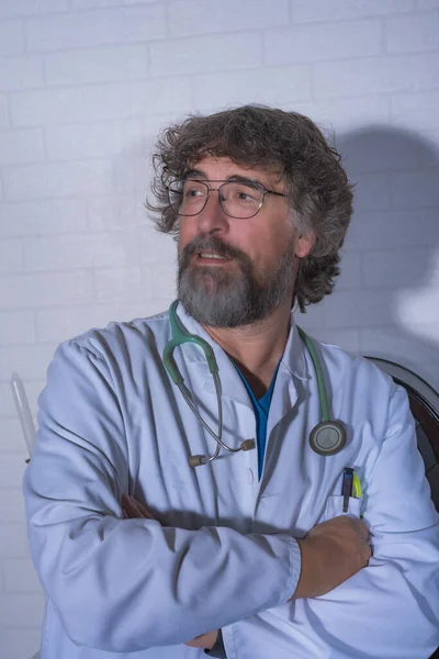 bearded doctor dressed in a blue operating room clothes and white coat resting next to an old radio and fireplace medical professions medicine and health