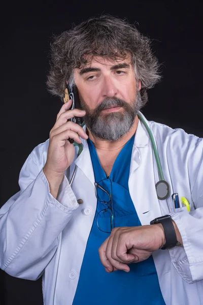 青い手術服を着たひげを生やした成熟した医者と心配そうな顔をした携帯電話で話す白いコート医療専門職 — ストック写真