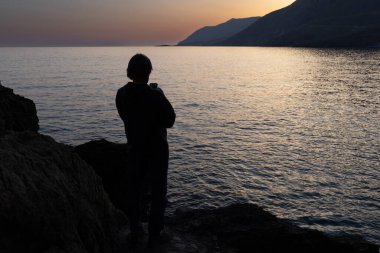Bir adam gün batımında Yunanistan, Girit, deniz kıyısında duruyor.